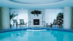 Une piscine intérieure avec une cheminée, deux fauteuils et des plantes en pot.