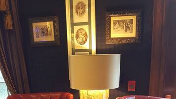 A room with a tufted leather armchair, a matching ottoman, and a round table. There is a wall-mounted lamp and framed pictures above the armchair.