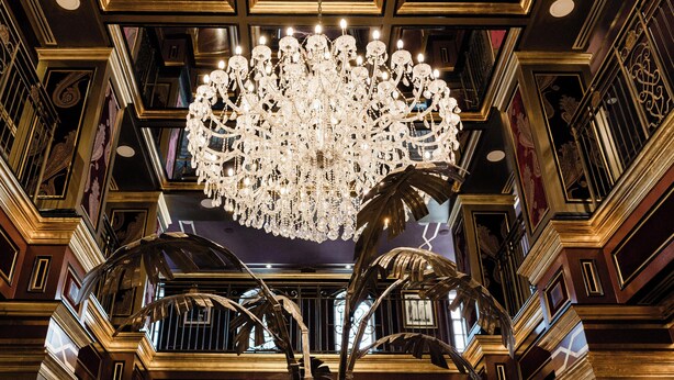 Un intérieur somptueux, agrémenté de lustres décoratifs, d’un grand miroir et d’un escalier.