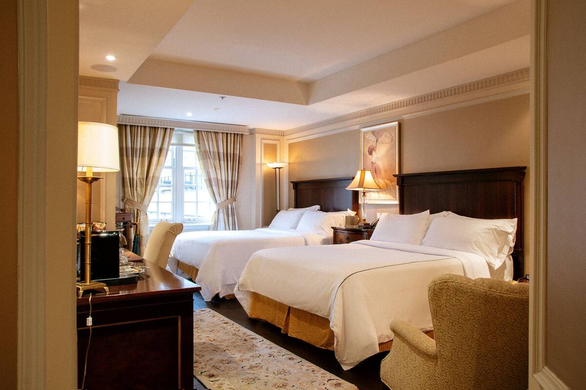 Une chambre d’hôtel avec deux lits, un bureau, une chaise et une grande fenêtre avec des rideaux.