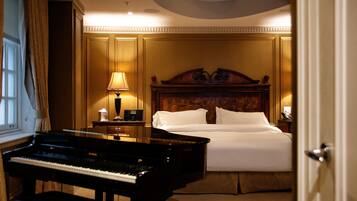 A hotel room with a grand piano, a neatly made bed, and a nightstand with a lamp.