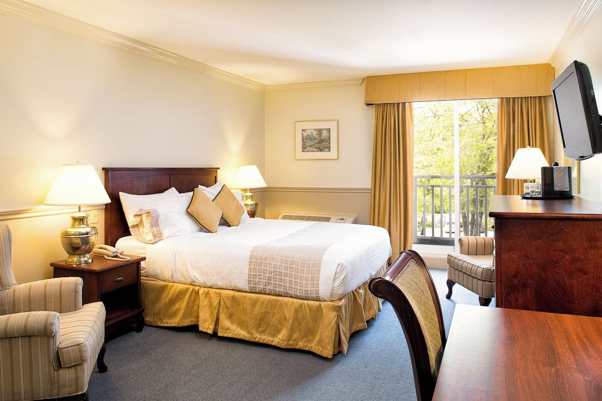 Ein Hotelzimmer mit einem großen Bett, zwei Nachttischlampen, einem Sessel, einem Schreibtisch und einem Fernseher.