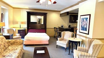 Una habitación de hotel con cama, sofá, sillón, mesita, ventilador de techo y zona de cocina.