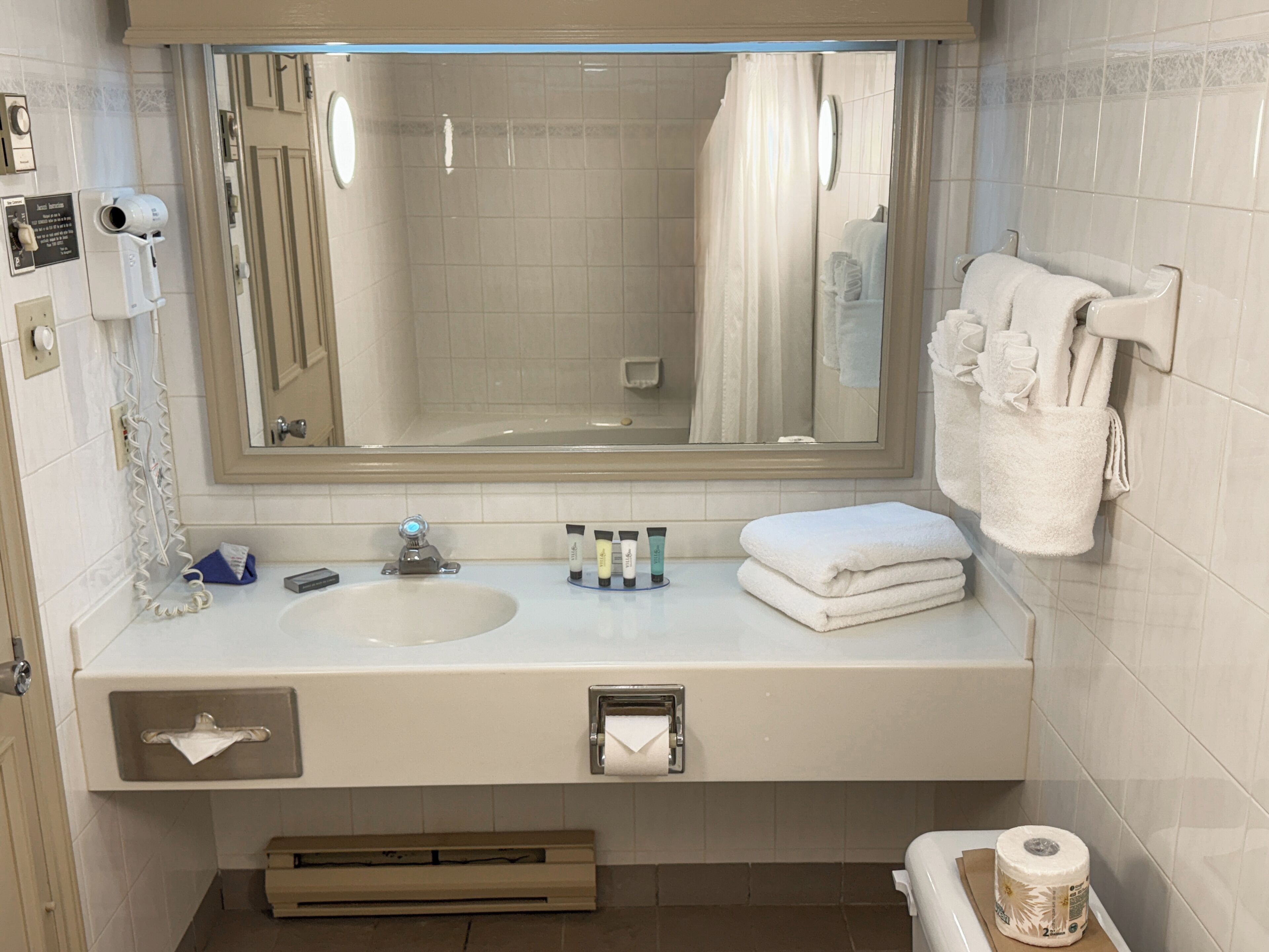 A bathroom with a large mirror, two sinks, a towel rack, and a toilet paper holder.
