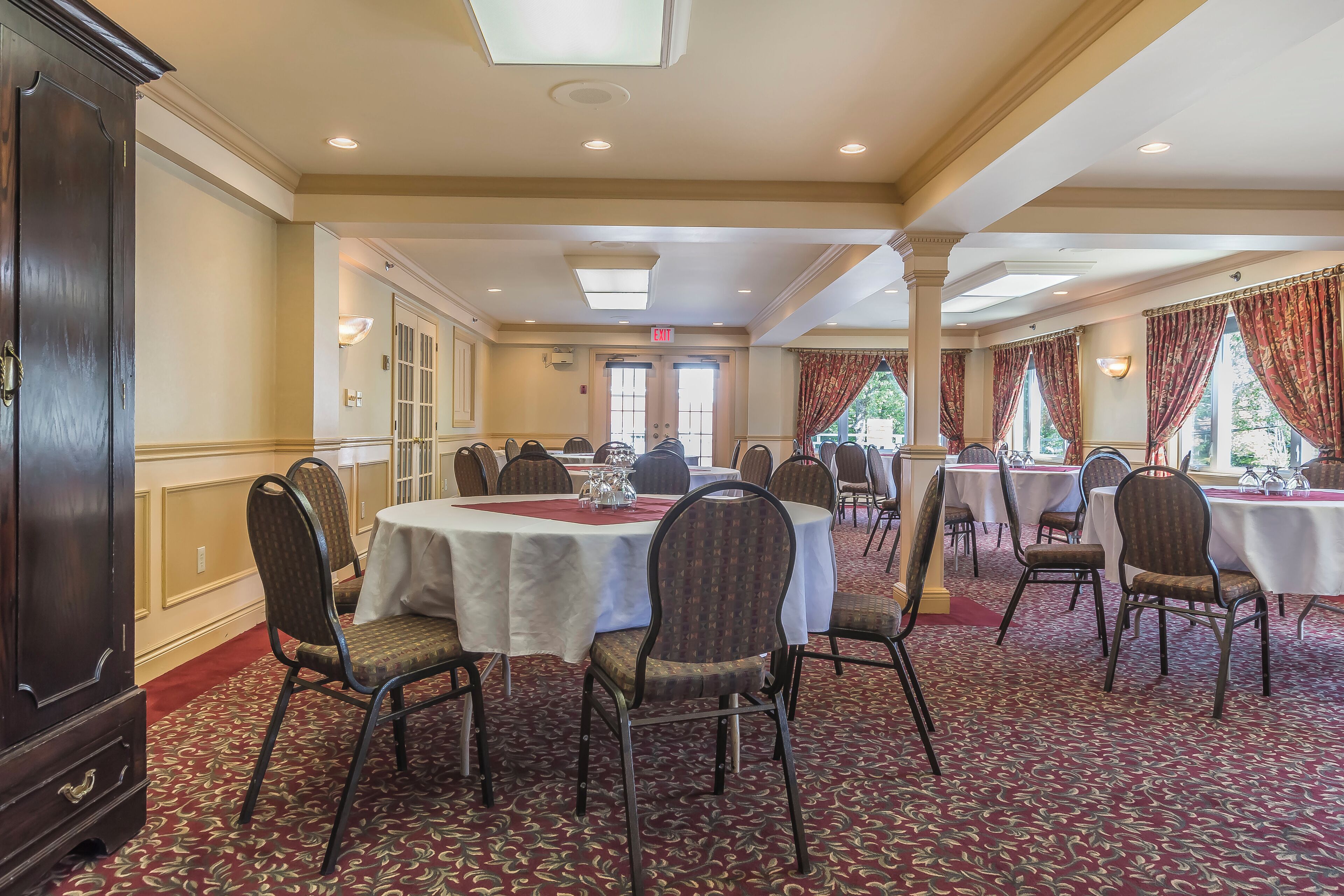 A banquet hall with round tables, chairs, and a carpeted floor.