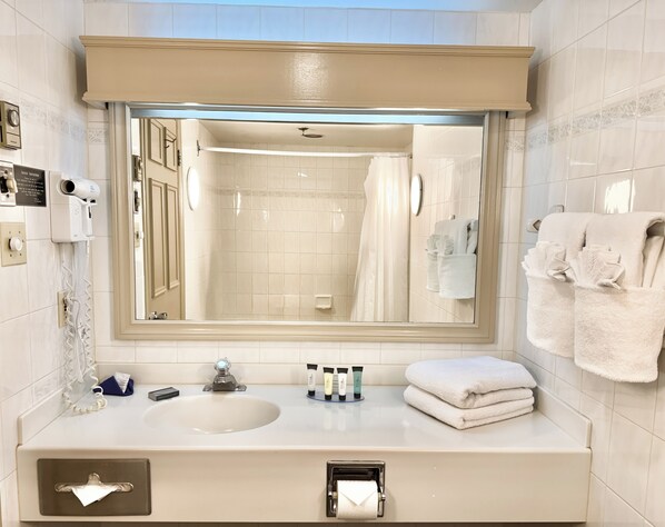 A bathroom with a large mirror, a sink, a towel rack, and a hairdryer.
