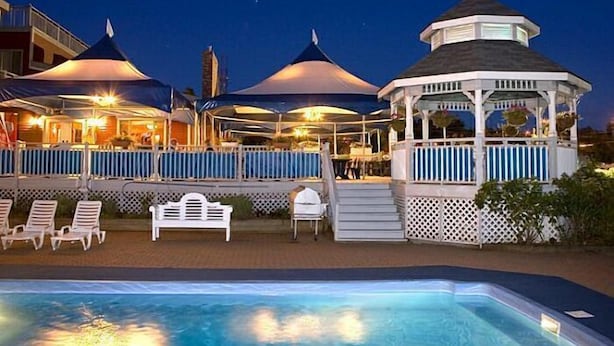 A poolside area with lounge chairs and umbrellas, a gazebo, and a building with multiple levels and outdoor seating. - Inn on the Lake (Fall River)