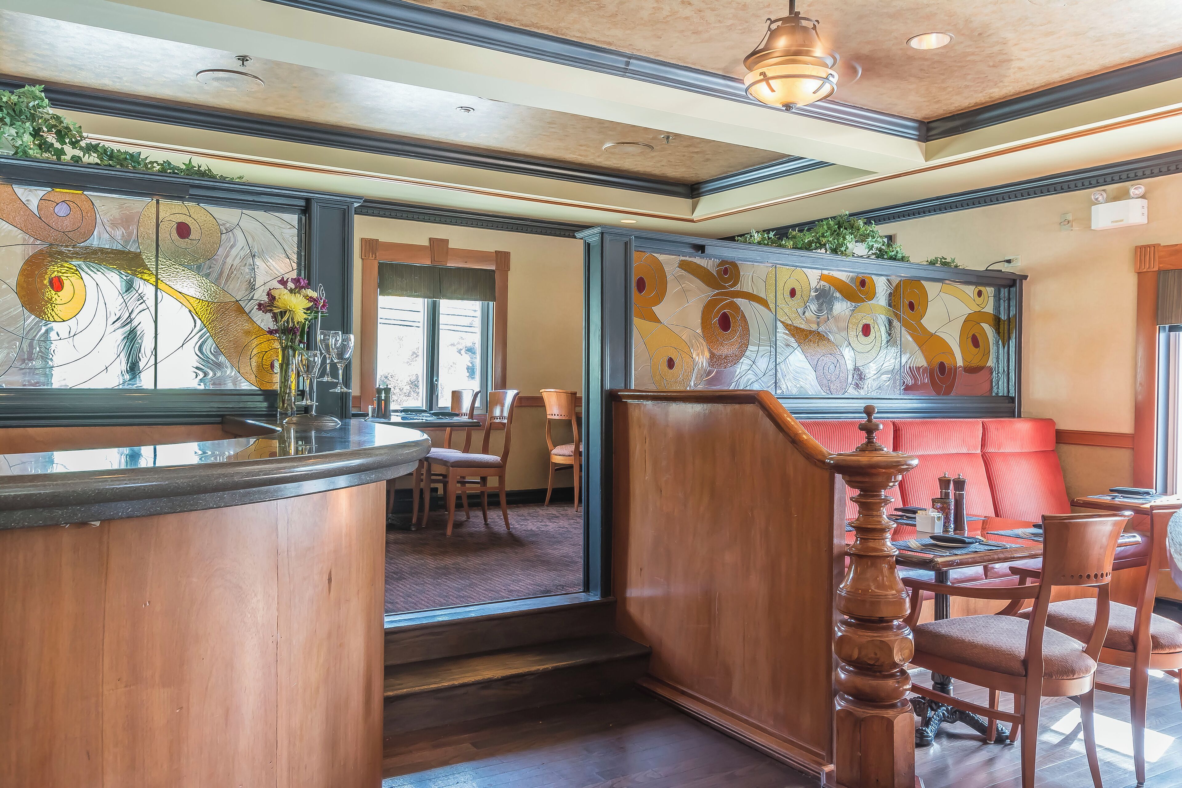 A restaurant interior with a wooden bar, red cushioned seating, and a decorative wall with abstract art.