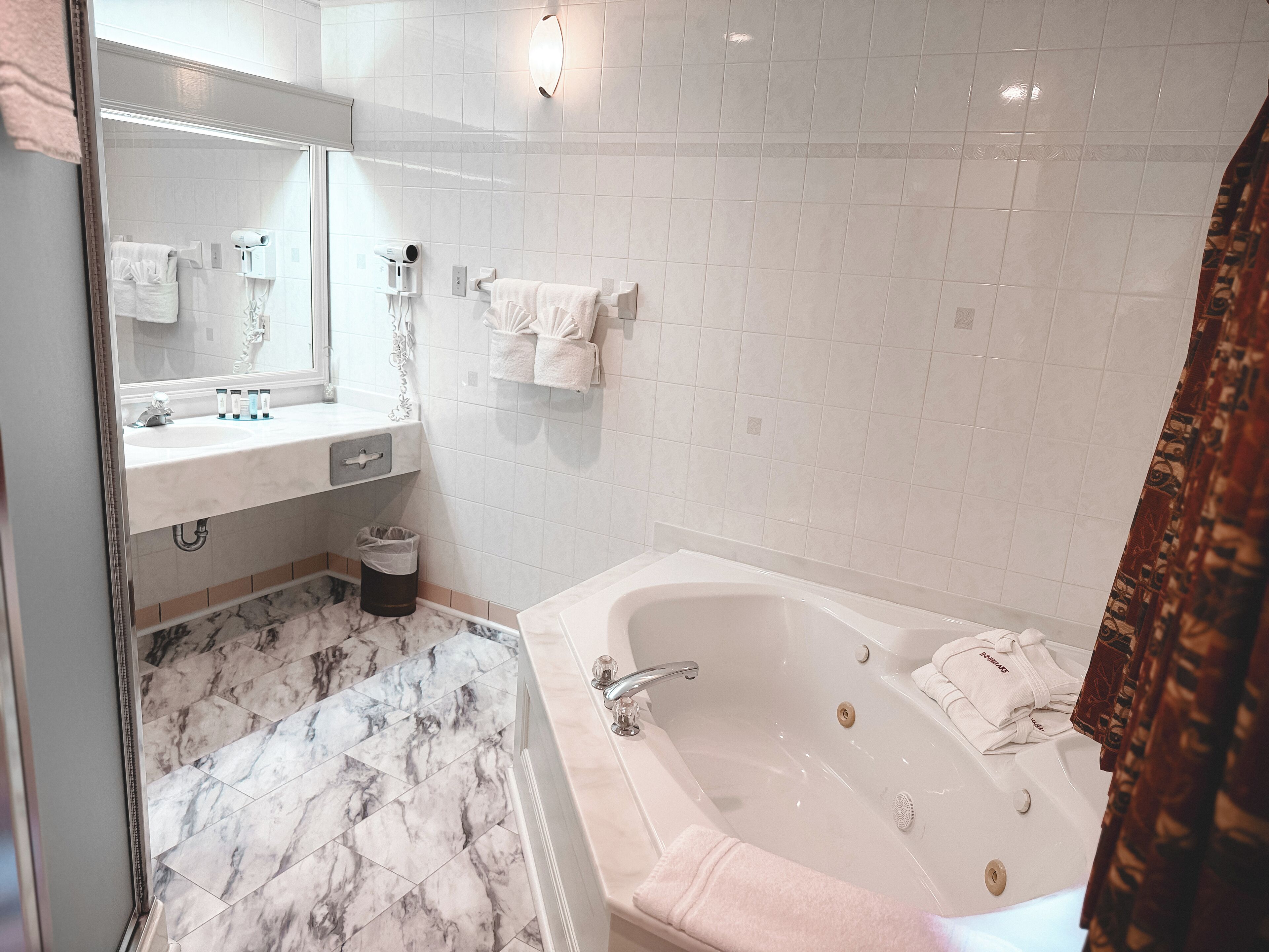 A bathroom with a marble floor, a white bathtub, a sink with a mirror, and a towel rack.