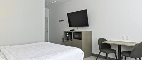 A modern hotel room with a bed, a desk with two chairs, a flat-screen TV, and a coffee machine.