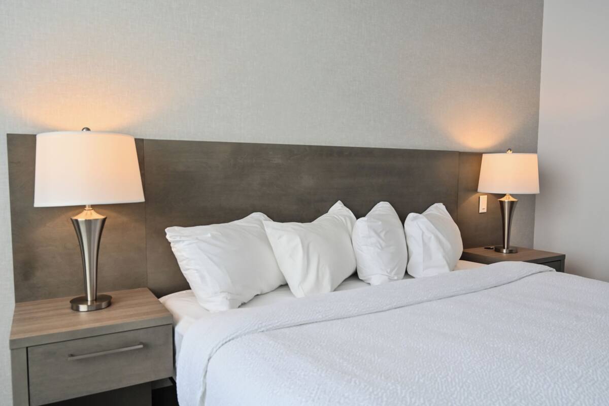 A neatly made bed with white bedding, two bedside lamps, and a modern headboard.