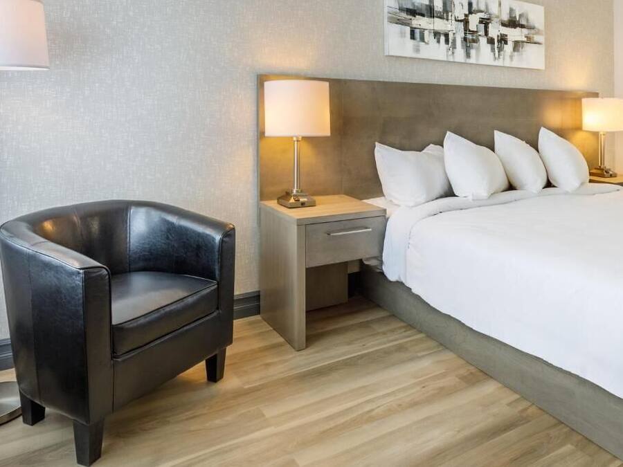 A hotel room with a bed, a chair, a nightstand, and a lamp.