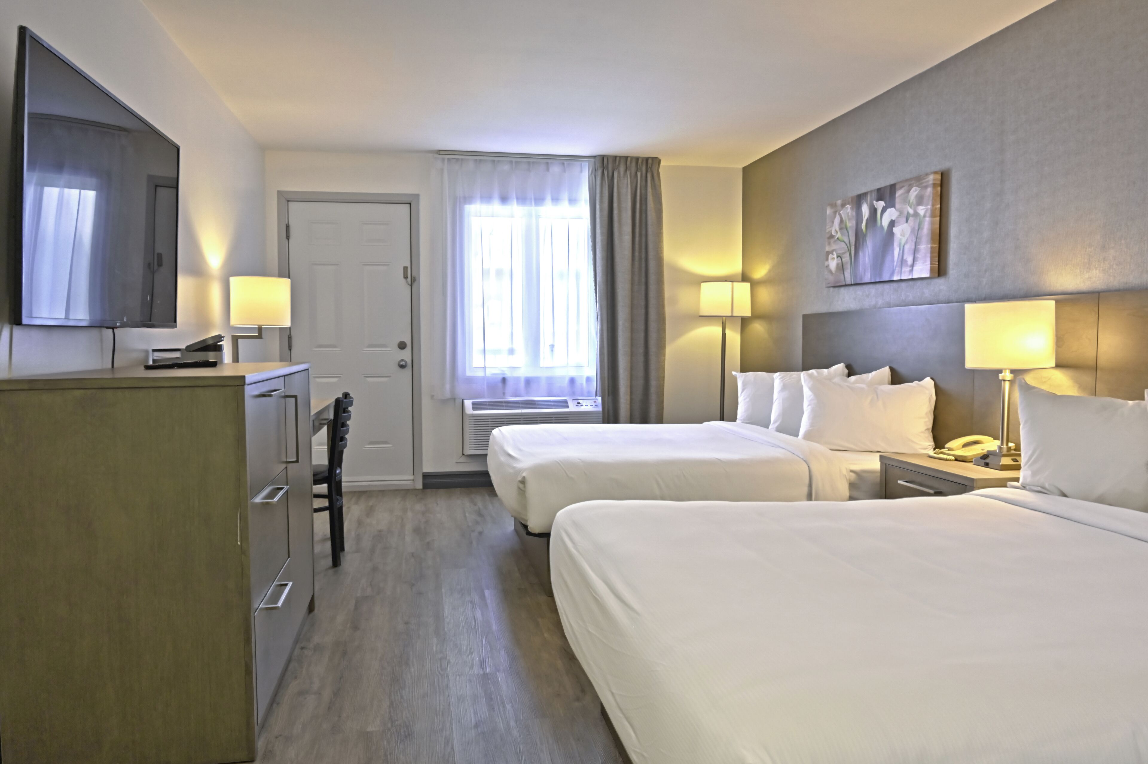 Habitación de hotel con dos camas, un escritorio, un televisor, una puerta y una ventana con cortinas.