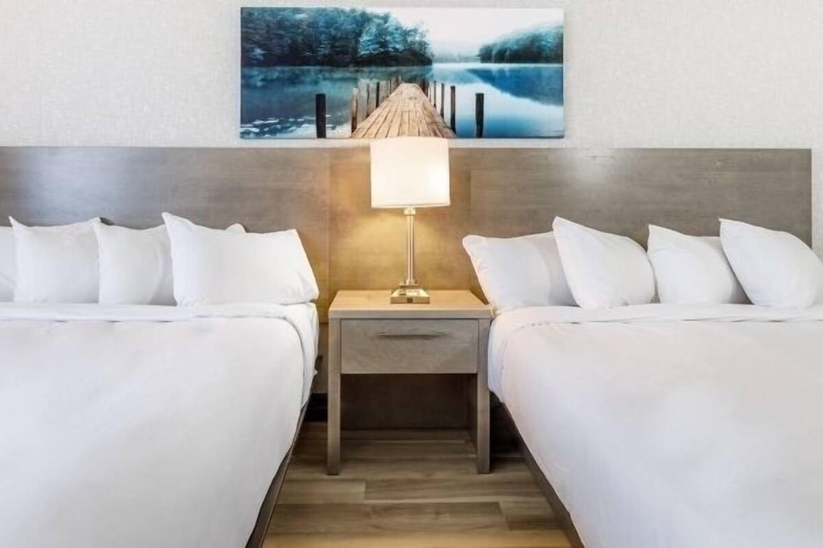 A hotel room with two beds, a nightstand with a lamp, and a painting of a pier.