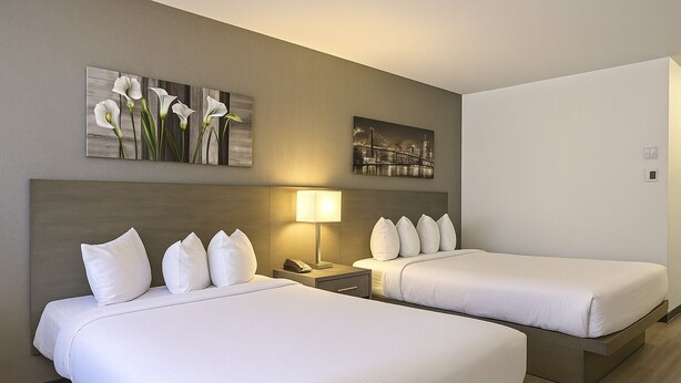 Une chambre d’hôtel avec deux lits, une table de chevet, une lampe et deux œuvres d’art murales.