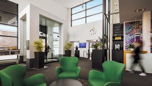 A modern lobby with green chairs, a reception desk, and a coffee bar. - Hôtel Alt Québec (Québec City)