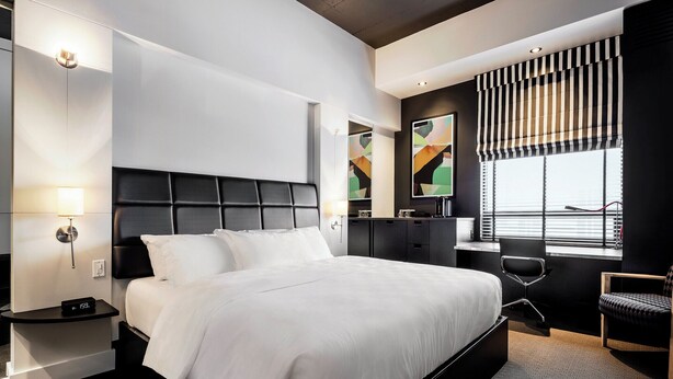 A modern hotel room with a large bed, bedside tables, a desk, and a window with blinds. - Hôtel Alt Québec (Québec City)
