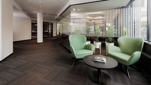 A modern office lobby with two green chairs, a round table, and a glass partition with vertical blinds. - Hôtel Alt Québec (Québec City)