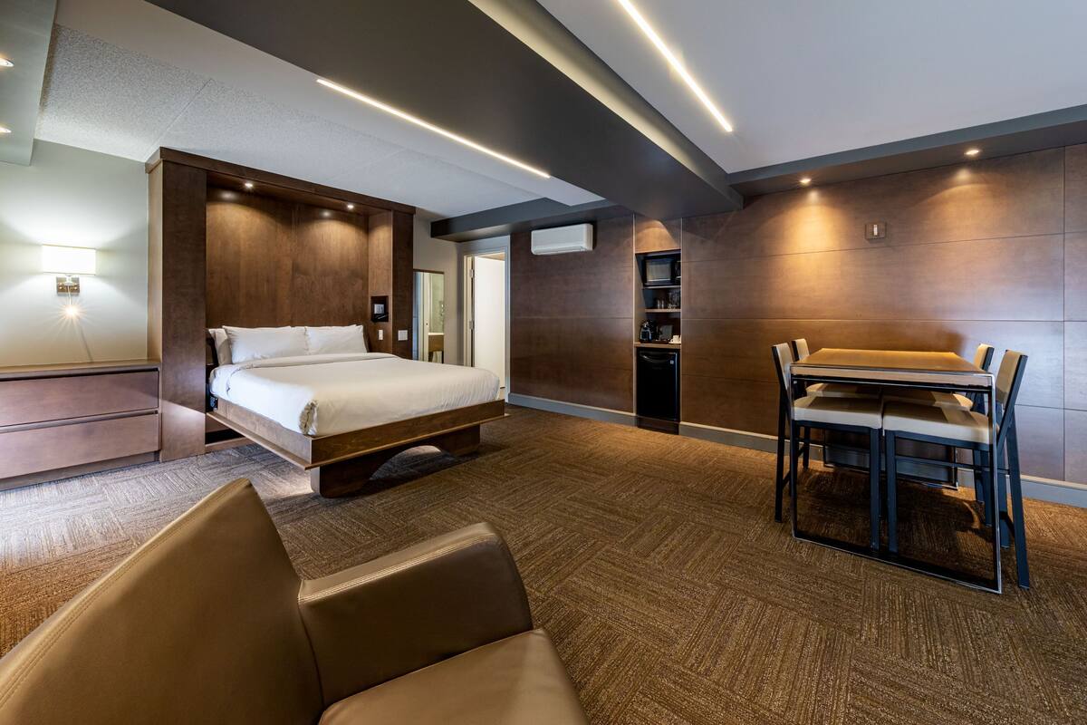 A modern hotel room with a large bed, a desk with a chair, and a built-in wardrobe.