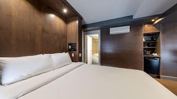 Una habitación de hotel moderna con una cama grande, cabecera de madera integrada y una cocina con microondas y cafetera.