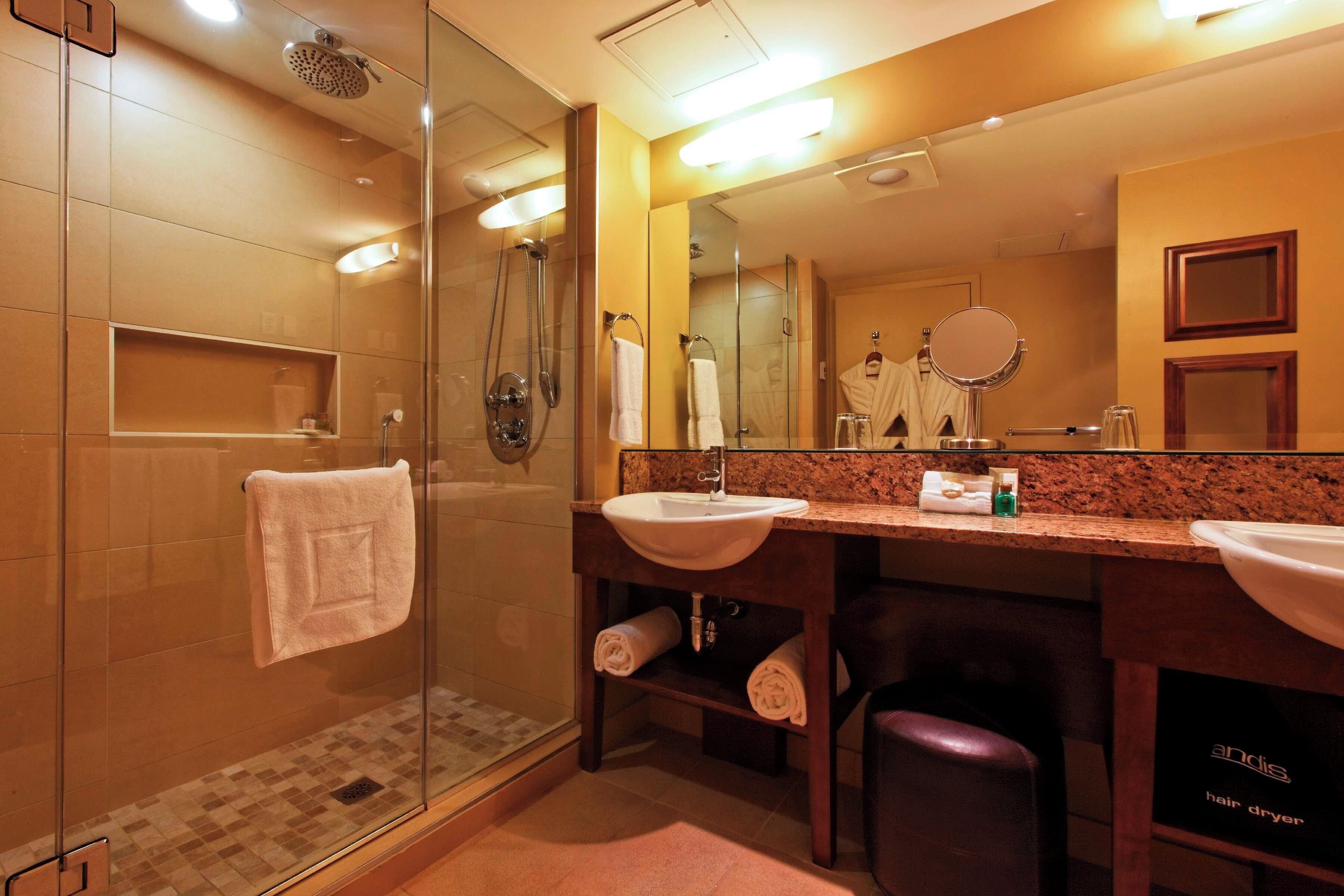A modern bathroom with a glass-enclosed shower, two sinks, a hair dryer, and a mirror.