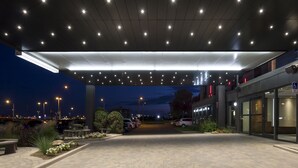 A hotel entrance with a covered walkway, outdoor seating, and a parking area. - Hôtel & Suites Normandin Quebec (Québec City)