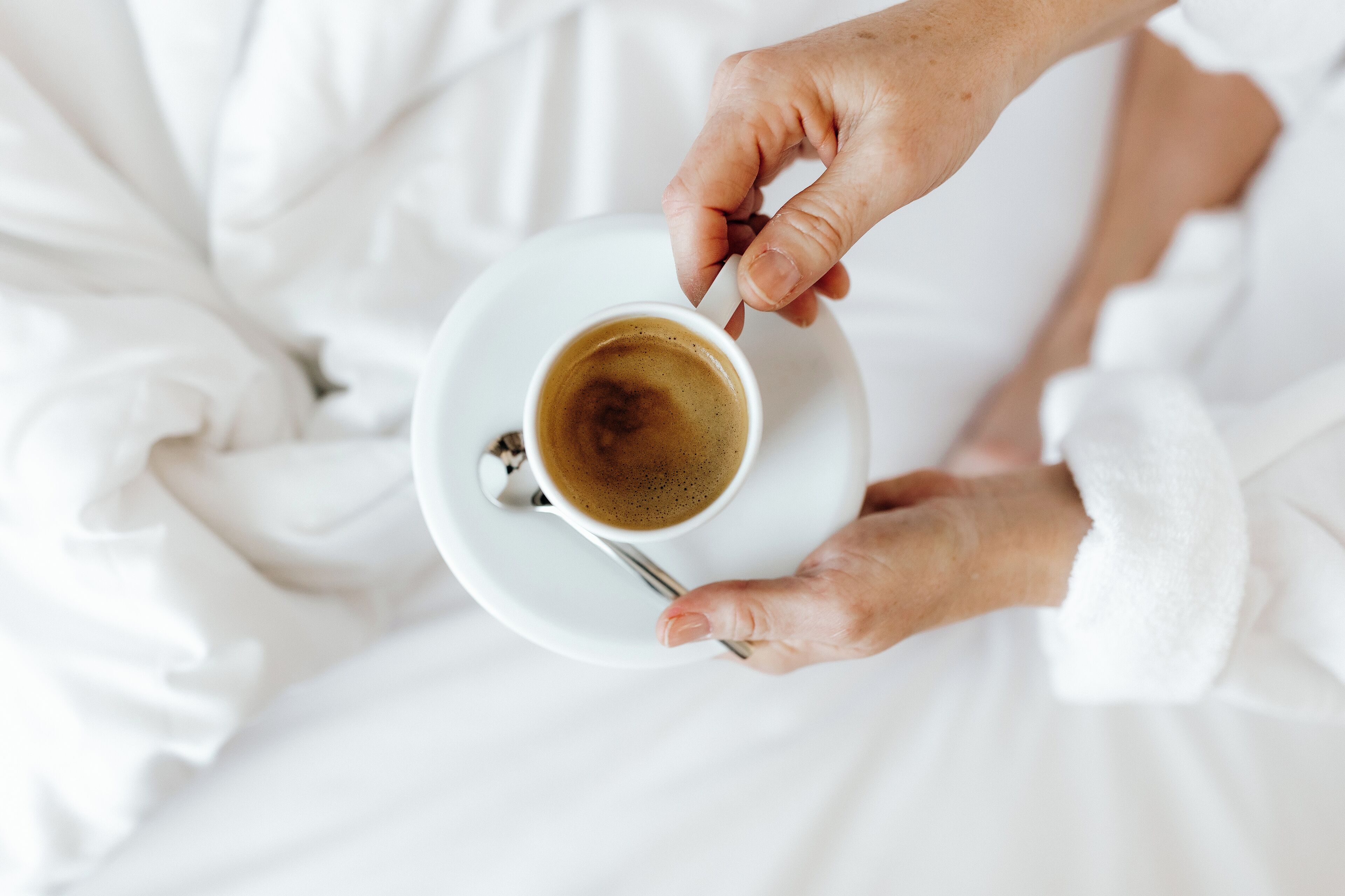 Une personne tenant une tasse de café sur une assiette blanche.
