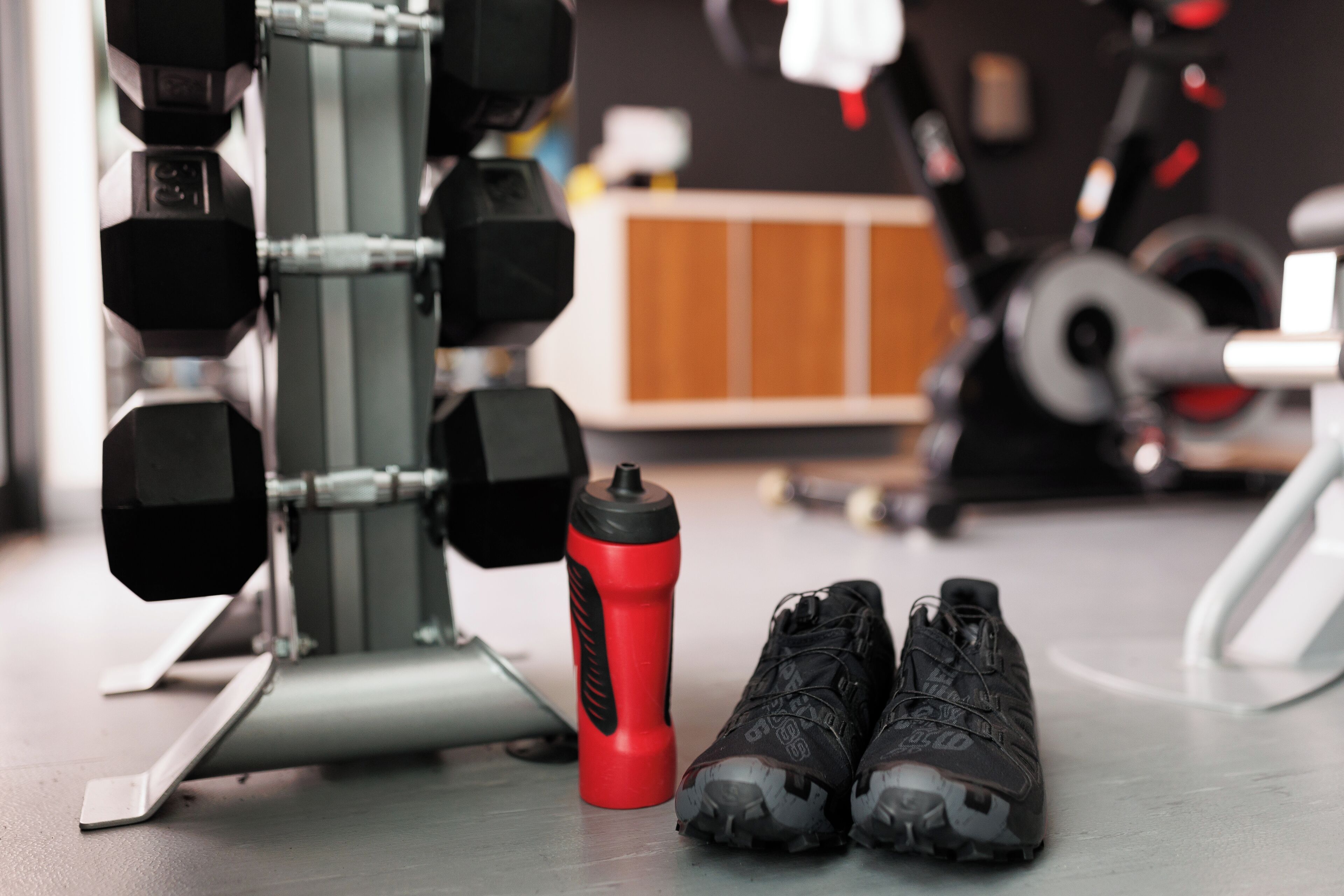 A pair of hiking boots, a red water bottle, and a weightlifting bench in a gym setting.