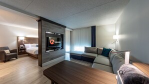 A modern hotel room with a flat-screen TV, a sofa, a bed, and a wooden coffee table. - Hôtel & Suites Normandin Quebec (Québec City)
