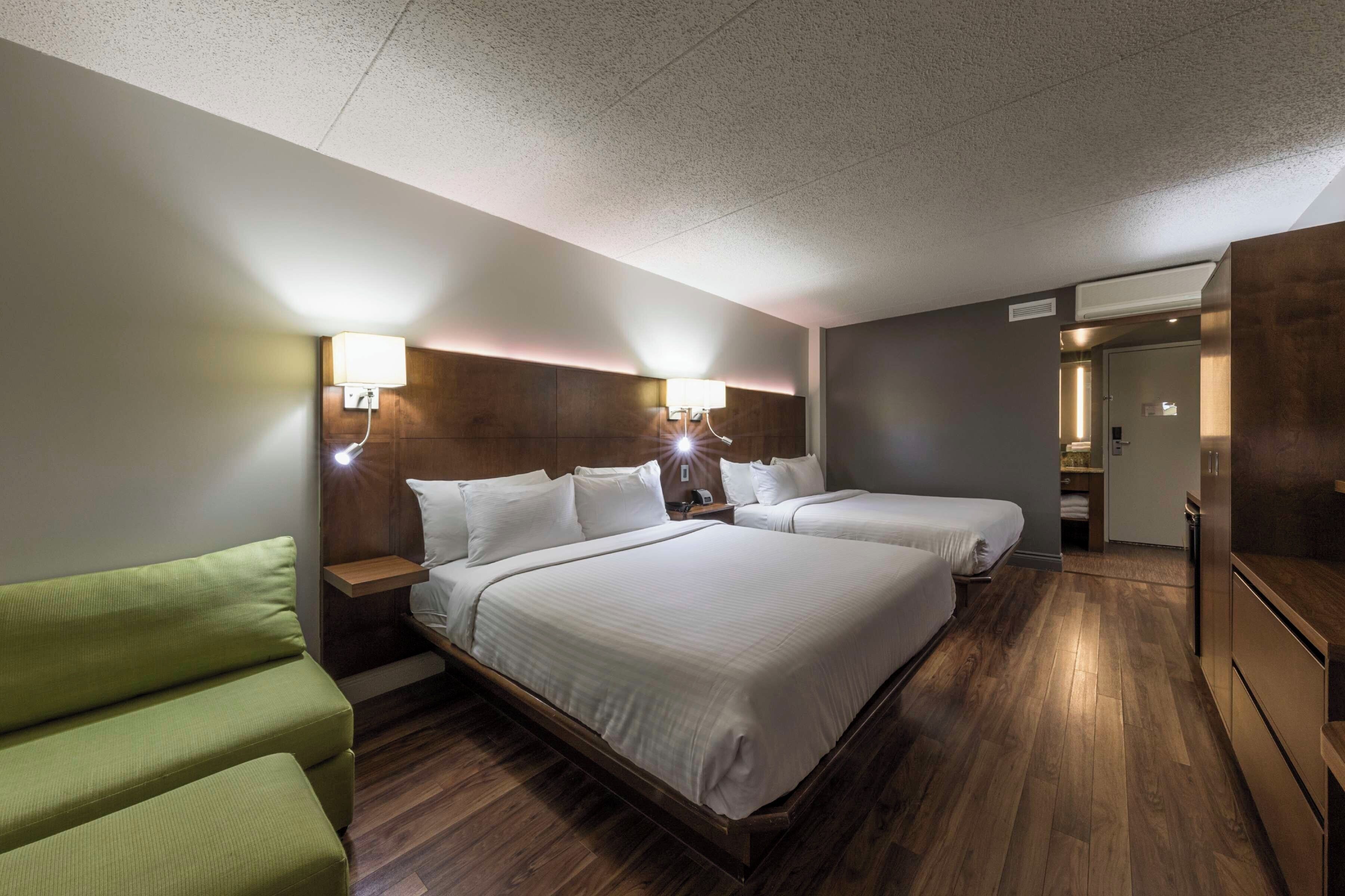 A hotel room with two beds, a green sofa, wooden flooring, and a modern design.