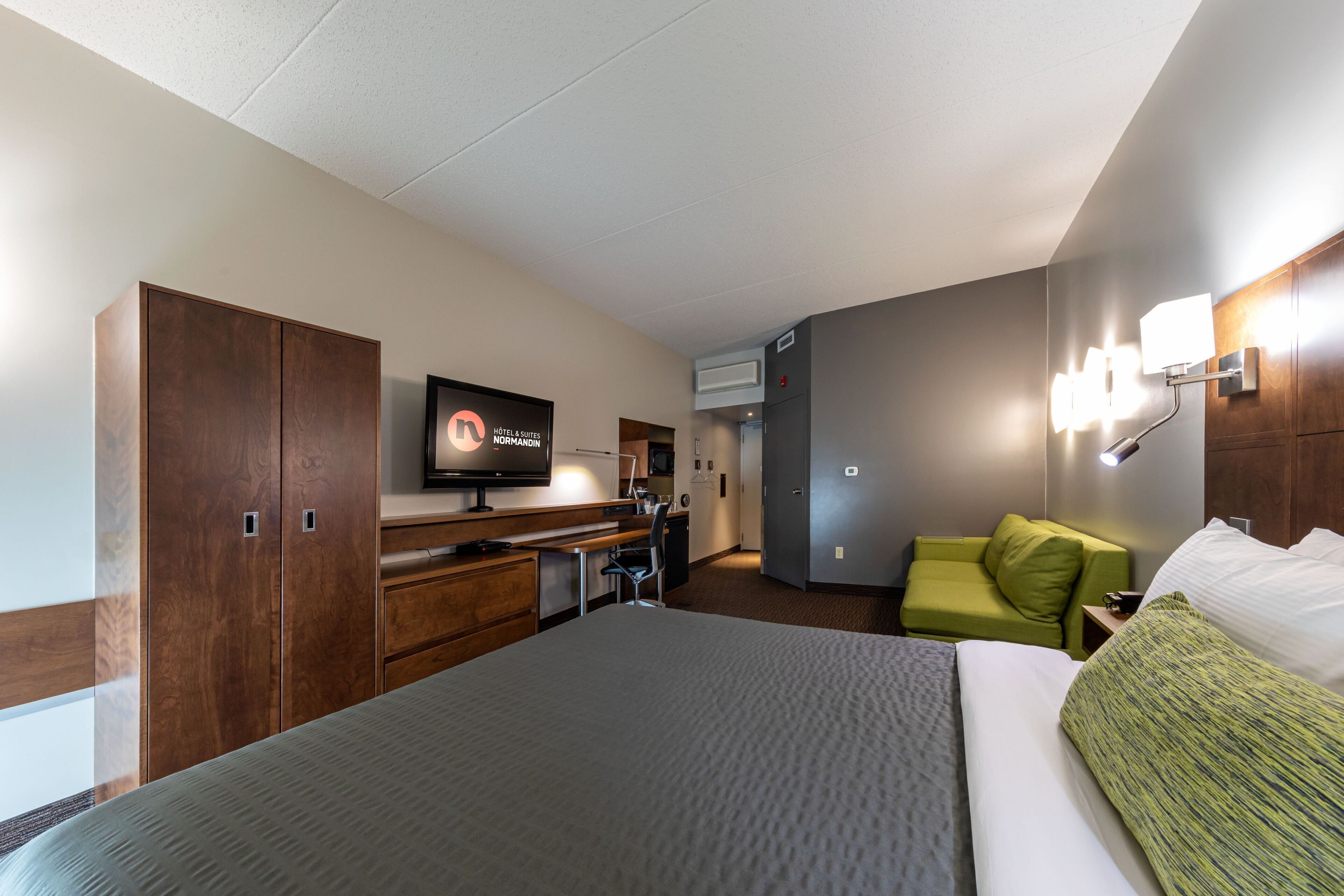 Una habitación de hotel con una cama, un escritorio, un televisor y un sofá verde.