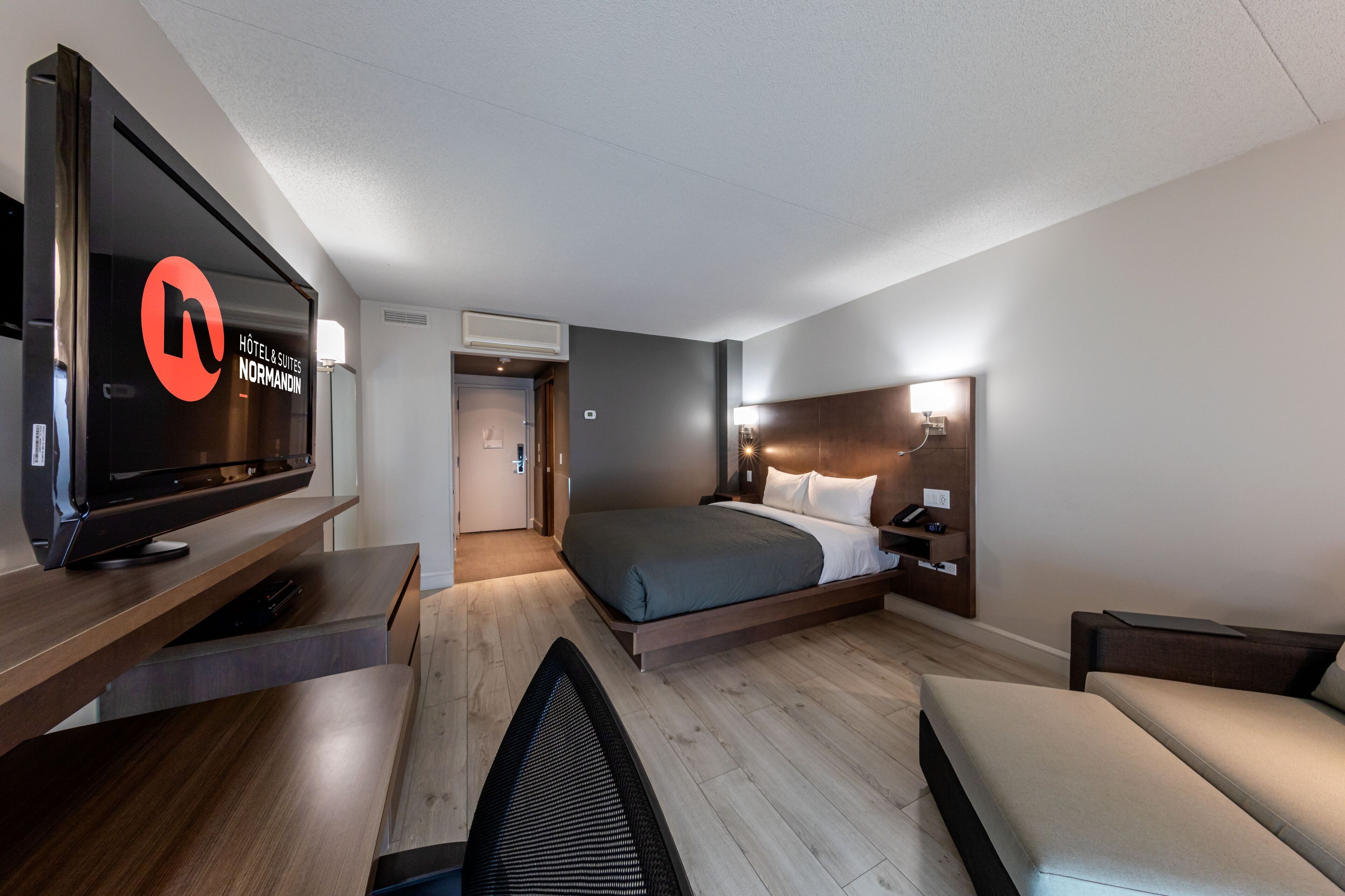 Quarto de hotel moderno com cama, mesa de cabeceira, televisão e escrivaninha com cadeira.