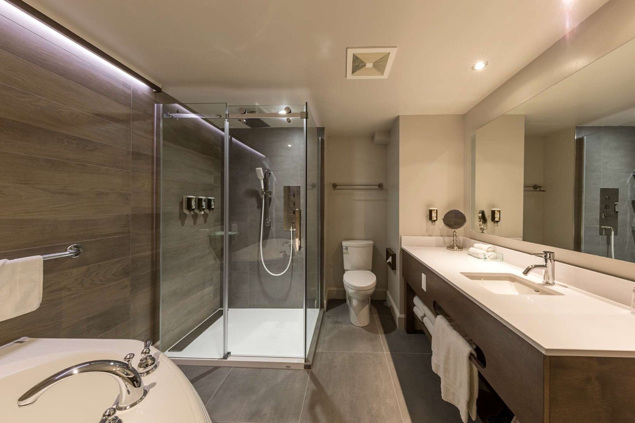 Un baño moderno con ducha envuelta en vidrio, un lavabo blanco y un espejo grande.