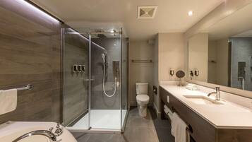 Un baño moderno con ducha envuelta en vidrio, un lavabo blanco y un espejo grande.