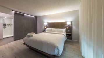 Una habitación de hotel moderna con una cama grande, mesitas de noche, ducha integrada y baño tipo suite.