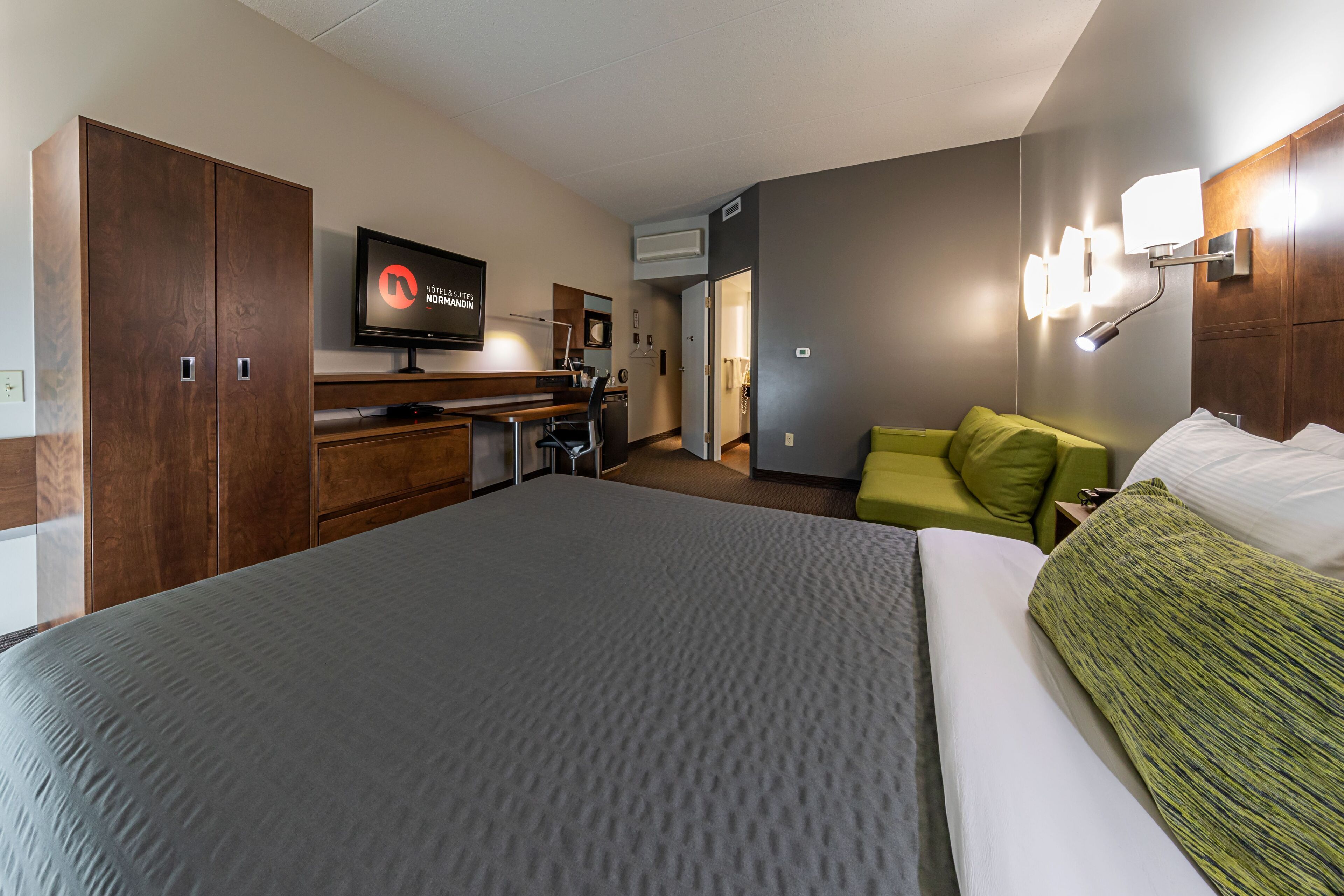 A hotel room with a large bed, a desk with a chair, a television, and a green sofa.