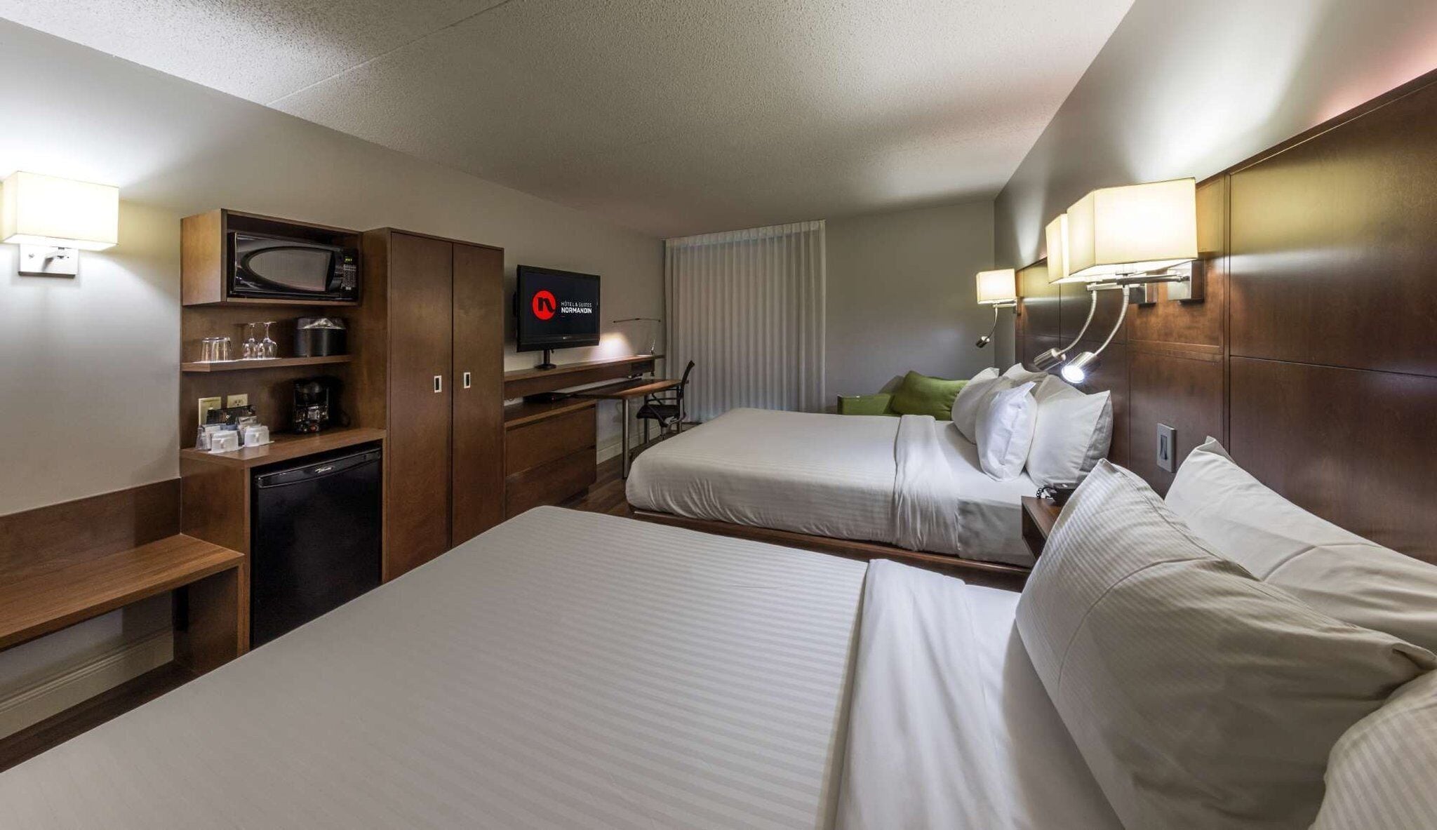 A hotel room with two beds, a television, a minibar, and a desk with a chair.