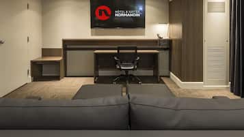Une chambre d’hôtel avec un grand téléviseur fixé au mur, un bureau avec une chaise et un canapé.