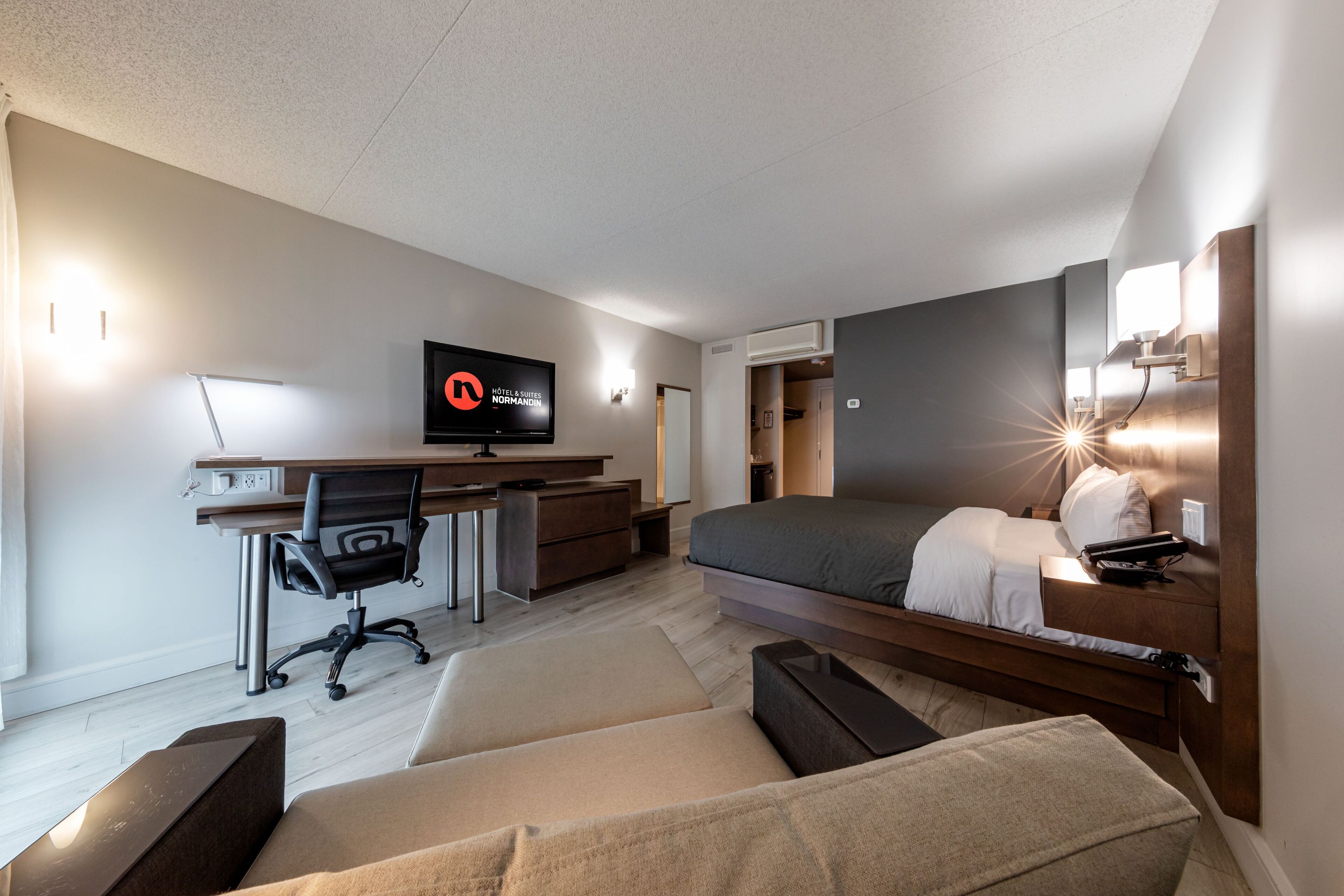 A modern hotel room with a bed, desk, chair, and a TV.