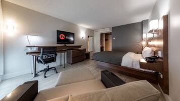 A modern hotel room with a bed, desk, chair, and a TV.