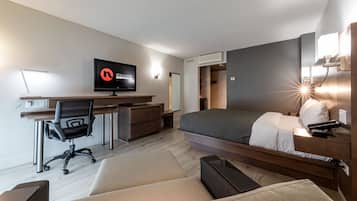 A modern hotel room with a bed, desk, chair, and television.