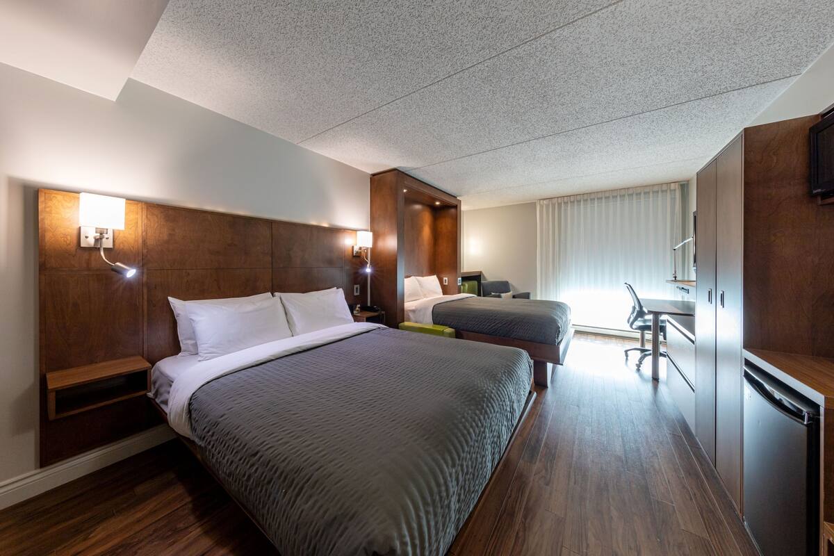 A hotel room with two beds, a desk, a chair, a TV, and a minibar.