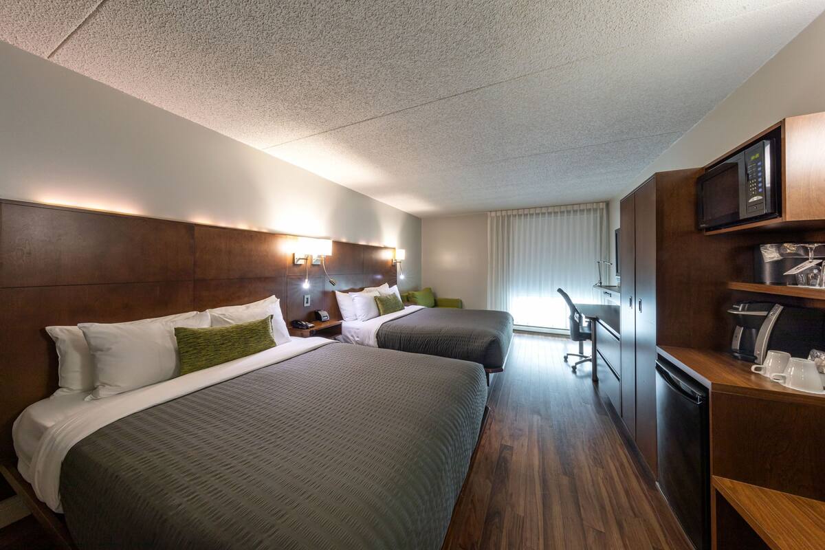 A hotel room with two beds, a desk, a microwave, and a coffee maker.
