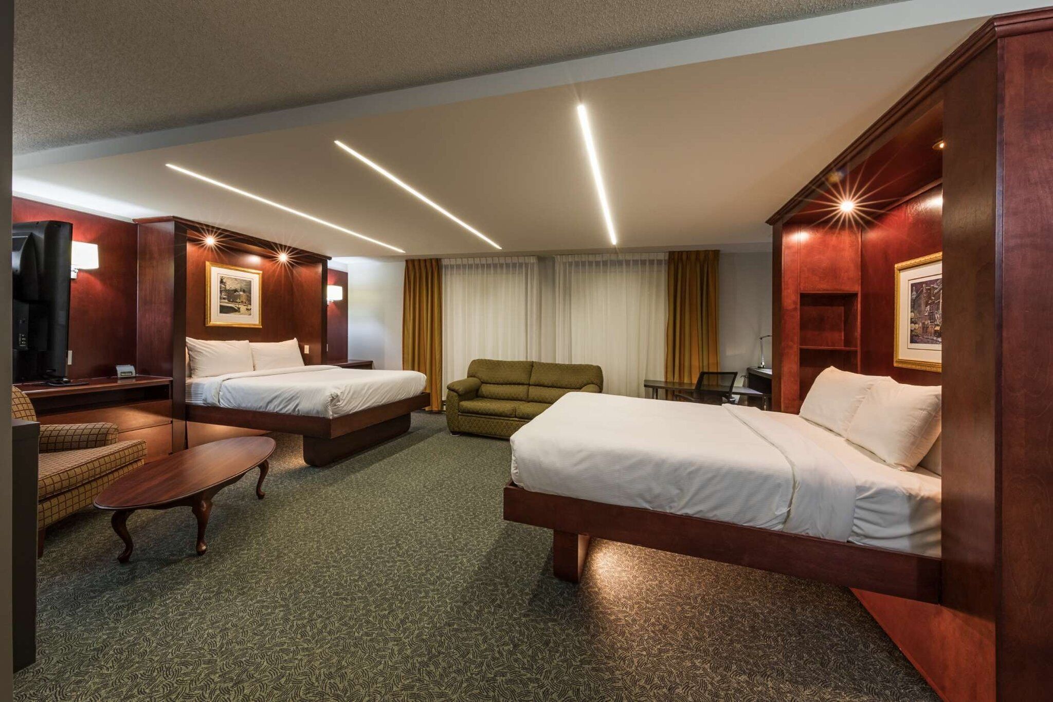 A hotel room with two beds, a sofa, a TV, and a desk.