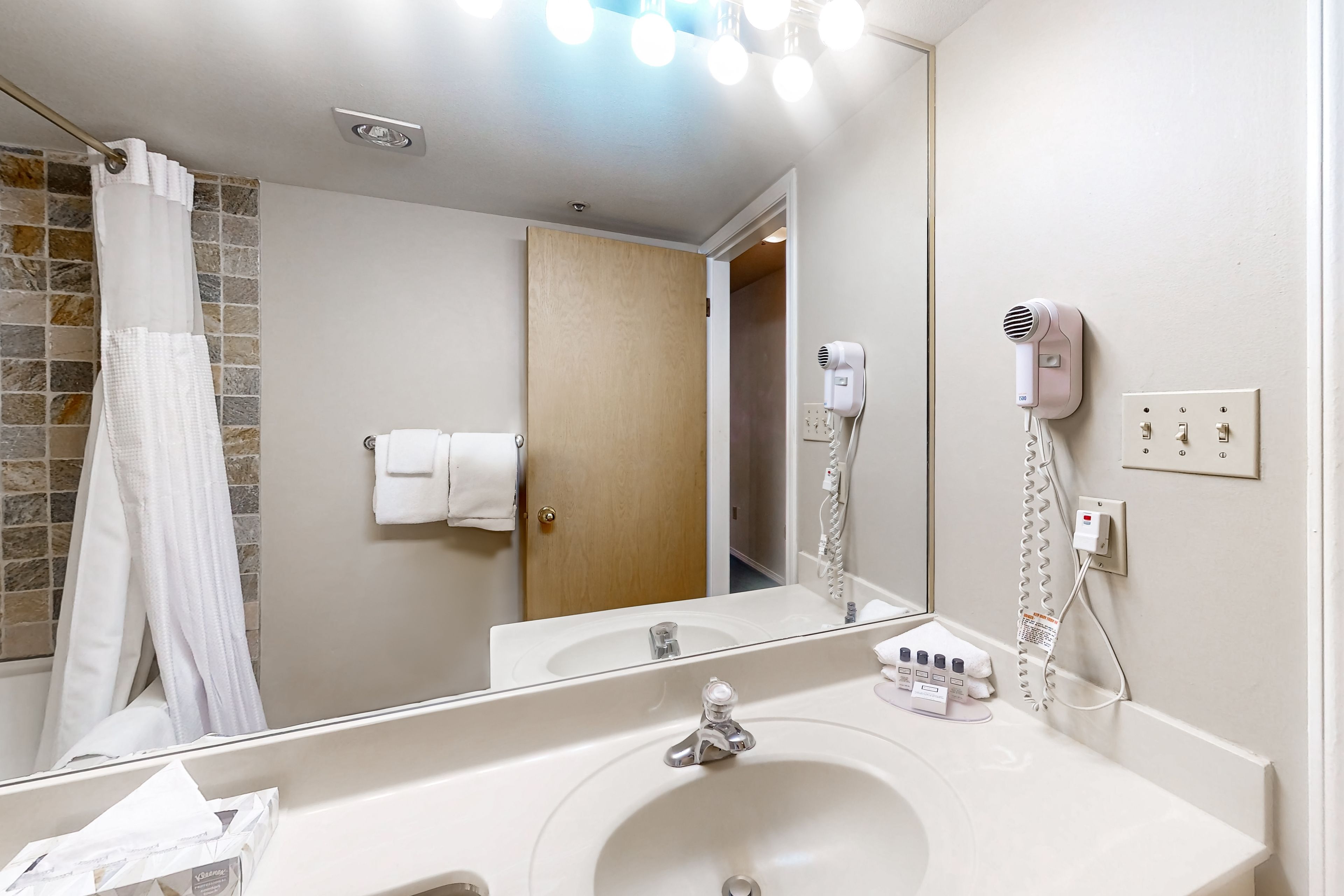 Une salle de bain équipée d’un lavabo, d’un miroir, d’un porte-serviettes et d’un sèche-cheveux fixé au mur.