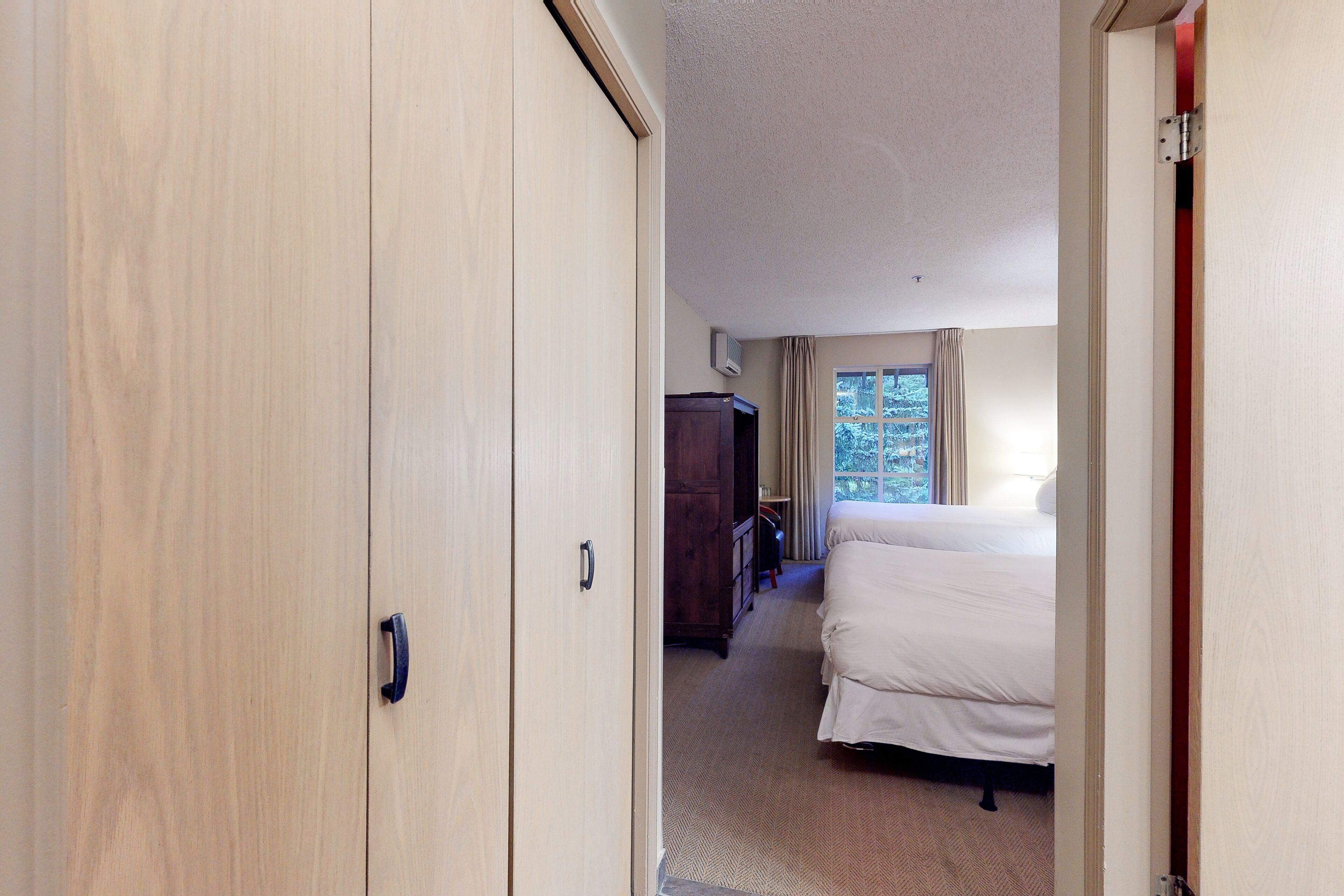Ein Hotelzimmer mit Holzschrank, Bett und einem fenster mit Vorhängen.