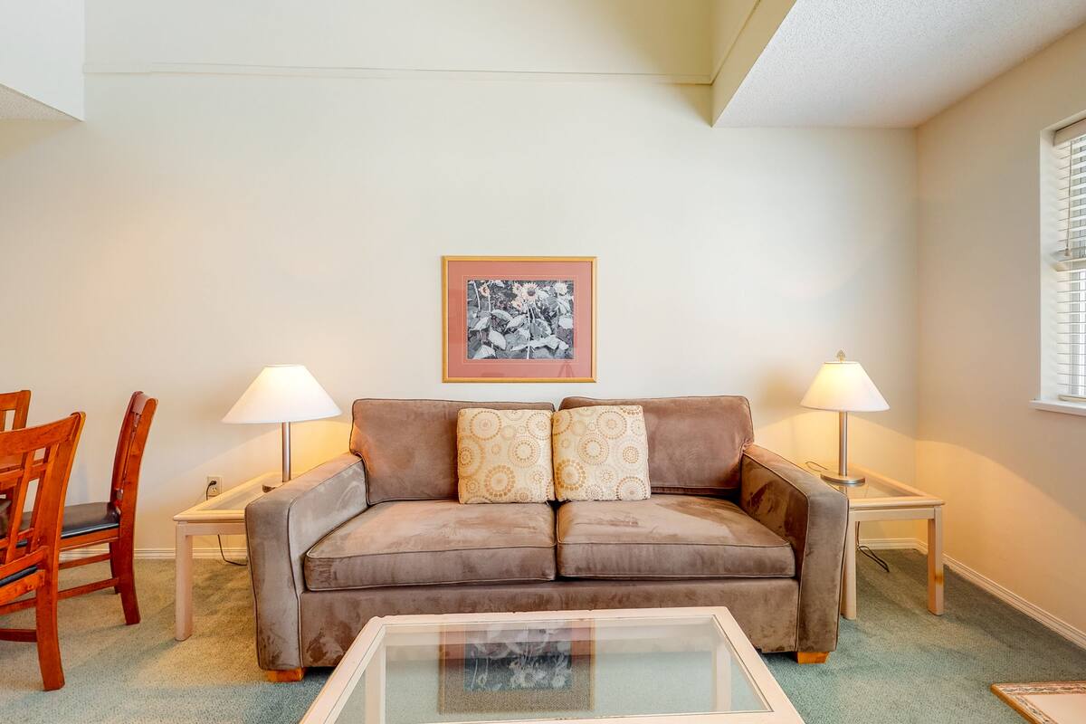 A living room with a brown sofa, two lamps, a framed picture on the wall, and a glass coffee table.