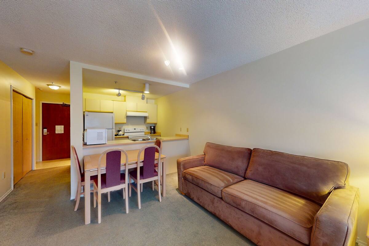 A compact living space with a kitchenette, a dining area with a table and chairs, and a brown leather sofa.