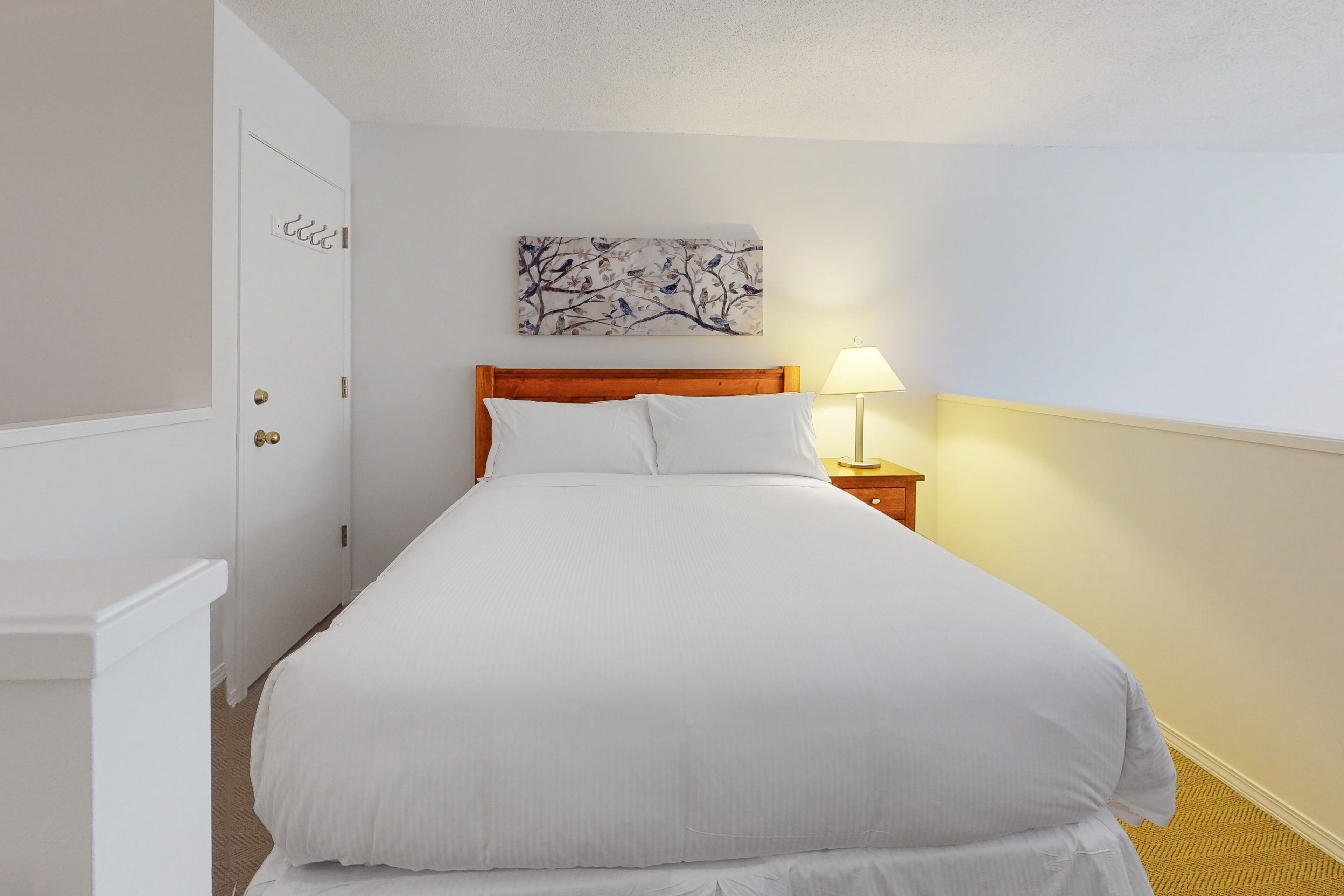 A neatly made bed with white linens, a wooden headboard, and a wall-mounted artwork above it.