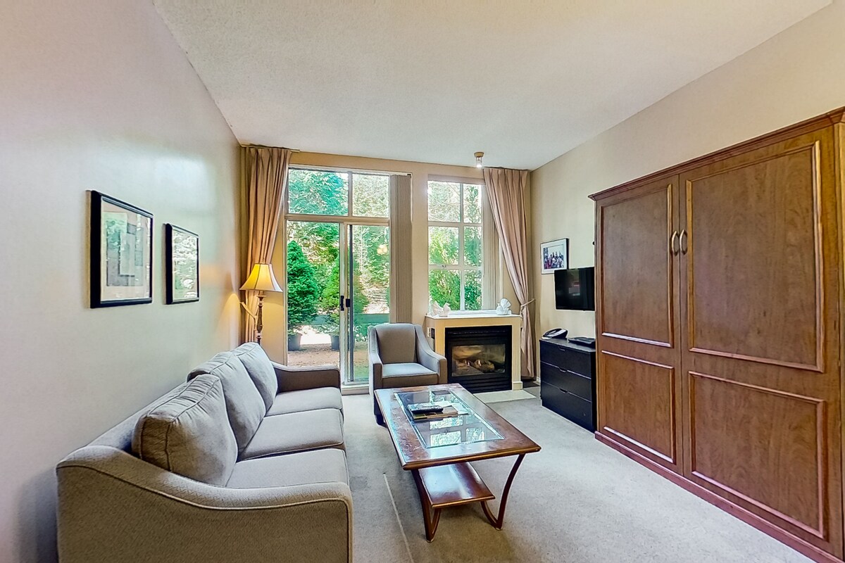 A living room with a sofa, a glass-top coffee table, a fireplace, and a large wooden wardrobe.